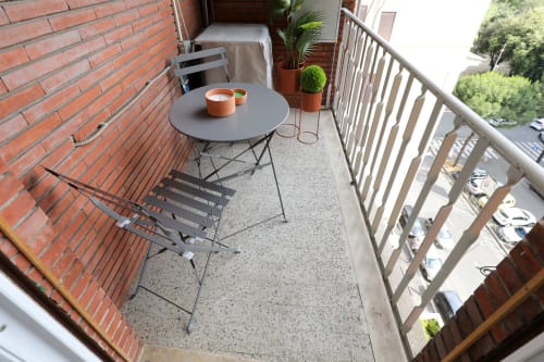 Accogliente balcone di appartamento a Roma con tavolo rotondo grigio, sedie e piante in vaso che si affaccia sulla strada