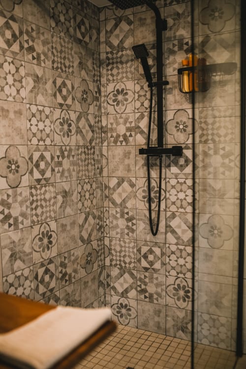 Salle de bain moderne avec carrelage motifs à l'hôtel ART DE VOYAGER à Étretat, équipée de robinetterie noire et cabine de douche vitrée