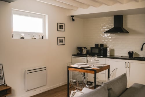 Cuisine-salle à manger moderne à Art de Voyager, Étretat avec meubles blancs, plan de travail noir et table en bois