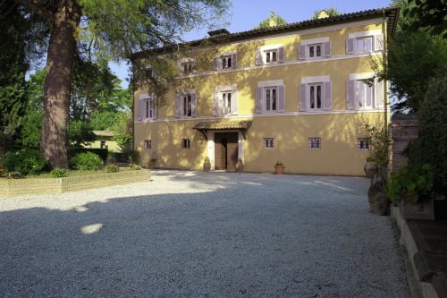 Villa Pandolfi Elmi, una villa gialla a Spello con persiane viola, cortile in ghiaia e alberi maestosi