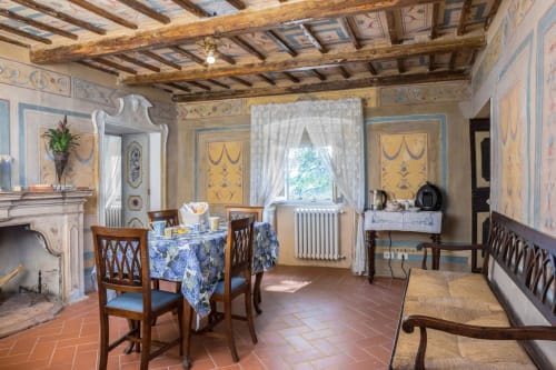 Sala da pranzo rustica di Villa Pandolfi Elmi a Spello con pareti affrescate, travi in legno, camino e arredi d'epoca.