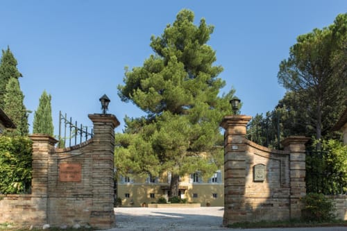 Ornato ingresso in pietra alla Villa Pandolfi Elmi a Spello, Italia, con cipressi e rustica villa sullo sfondo