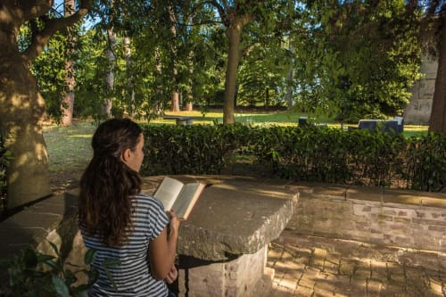 Ospite che legge all'aperto a Villa Pandolfi Elmi a Spello, Italia, sotto alberi ombrosi con giardini curati