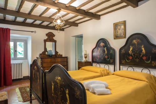 Elegante camera da letto di Villa Pandolfi Elmi a Spello con letto nero ornato, biancheria gialla, travi a vista e arredi d'epoca.