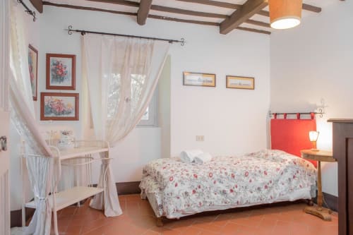 Affascinante camera da letto a Villa Pandolfi Elmi a Spello con biancheria floreale, travi a vista e arredamento rustico italiano.