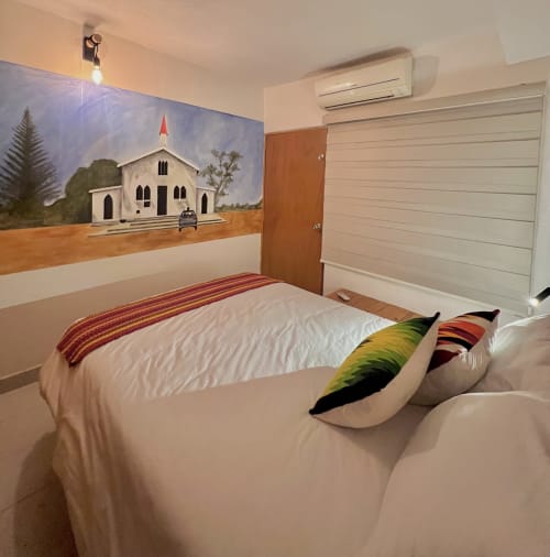 Dormitorio moderno en BajaReal Hotel Boutique con cama blanca, cojines coloridos y mural de iglesia en La Paz, México