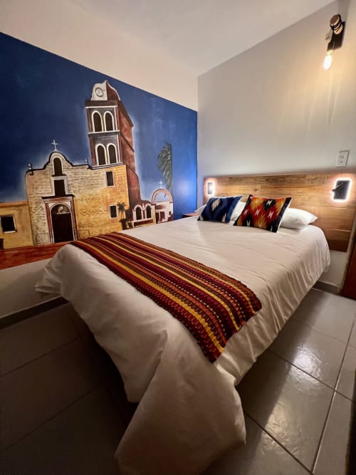 Habitación del BajaReal Hotel Boutique en La Paz con mural de iglesia colonial, cama blanca, ropa de cama a rayas y cabecero de madera.