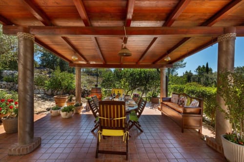 Zona pranzo sotto pergolato in legno a Villa Margherita con patio in cotto, tavoli e vista sul giardino mediterraneo