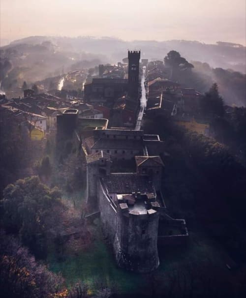 Corte Pincione medieval castle in misty Montecarlo, Italy surrounded by forested hills at dawn