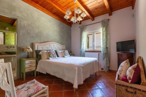 Elegante camera da letto a Villa Margherita con travi in legno, letto bianco, cuscini floreali e pavimenti in cotto a Santeramo in Colle