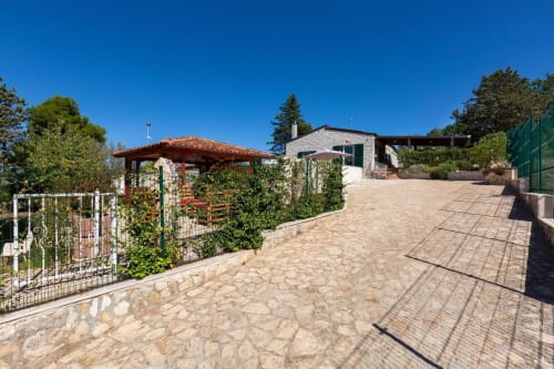 Corte pavimentata di Villa Margherita con pergolato, strutture ricoperte d'edera e edificio principale a Santeramo in Colle, Italia