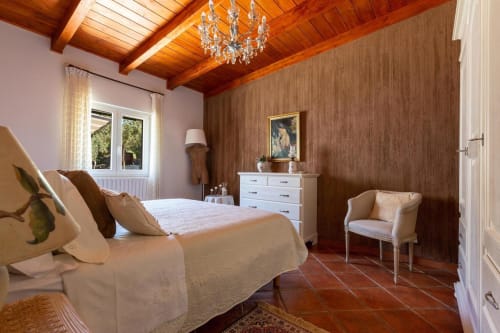 Elegante camera presso Villa Margherita con travi in legno, lampadario, arredamento bianco e pavimenti in cotto a Santeramo in