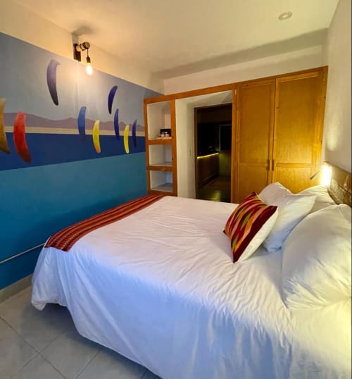 Habitación temática colorida en BajaReal Hotel Boutique, La Paz, con camas blancas, arte mural vibrante y muebles de madera