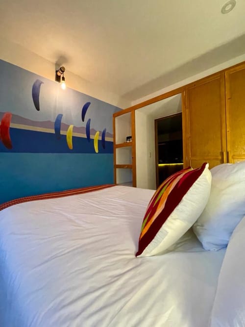 Habitación moderna del Hotel Boutique BajaReal en La Paz con mural colorido en la pared y almohadas de rayas rojas