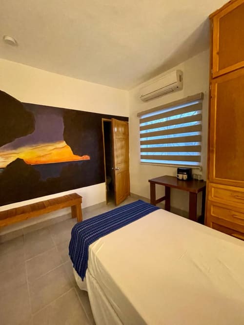 Habitación moderna en BajaReal Hotel Boutique de La Paz con cama, muebles de madera, aire acondicionado y cortinas enrollables a rayas