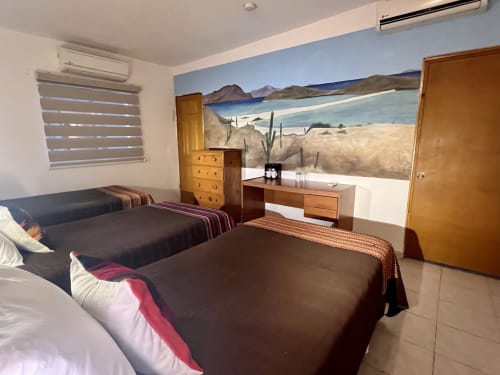 Espaciosa habitación de hotel en BajaReal Hotel Boutique en La Paz con dos camas, muebles de madera y mural desértico-playero