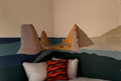 Habitación de hotel con mural costero, tres almohadas en la cama y diseño moderno en BajaReal Boutique, La Paz