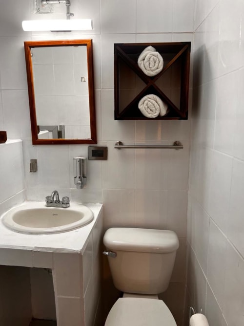 Baño moderno del Hotel Boutique BajaReal con lavamanos, inodoro, espejo y almacenamiento de toallas en La Paz