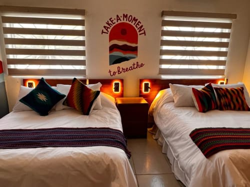 Camas gemelas con colchas coloridas en BajaReal Hotel Boutique en La Paz, con obras de arte al atardecer y cortinas rayadas