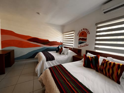 Habitación colorida del Hotel Boutique BajaReal en La Paz con dos camas, almohadas rayadas y mural de olas rojas en las paredes.