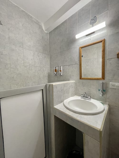 Baño moderno del Hotel Boutique BajaReal en La Paz con paredes de azulejos grises, lavamanos redondo y espejo con marco dorado