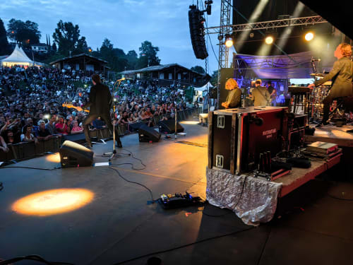 Outdoor concert stage at Les Chalets Du Lac De Montréjeau with crowd and lighting equipment at dusk