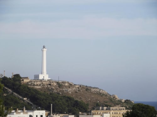 Faro bianco imponente sulla collina che domina il Mar Mediterraneo vicino a Leuca, Italia con palazzi residenziali sottostanti