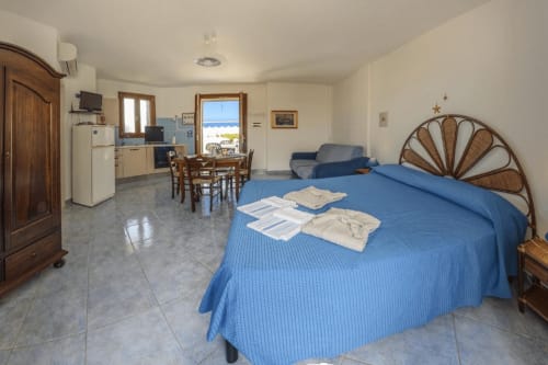 Monolocale con vista mare a Leuca: letto blu, angolo cottura, zona pranzo e balcone sulla costa