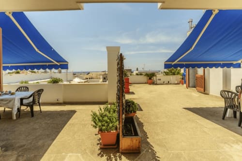 Terrazza sul tetto con tende azzurre, vista mare e piante in vaso ai Panoramici Monolocali di Leuca