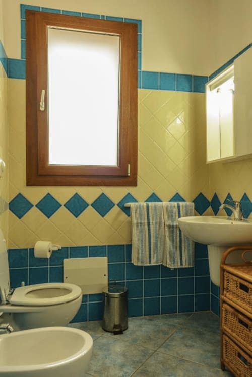 Bagno di Panoramici Monolocali a Leuca con piastrelle turchesi e gialle, lavabo, WC e mobile specchio in legno.