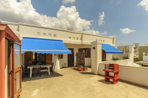 Terrazza soleggiata ai Panoramici Monolocali di Leuca con tenda blu, arredamenti bianchi e vista mare