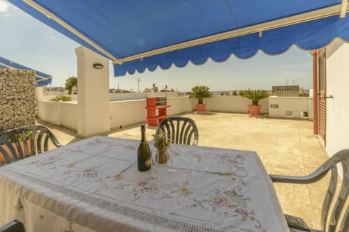 Terrazza con vista mare presso Panoramici Monolocali a Leuca, con tavolo da pranzo e tenda blu