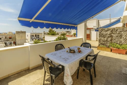 Terrazza panoramica ai Monolocali di Leuca con tenda blu, tavolo da pranzo e vista sul mare