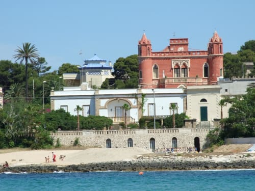 Villa affacciata colorata a Leuca con torre rossa e giardini mediterranei sul mare turchese