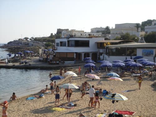 Spiaggia Panoramici Monolocali a Leuca con litorale sabbioso, ombrelloni blu e edifici fronte mare