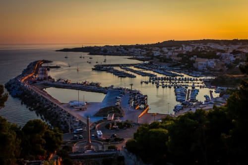 Vista al tramonto del porto di Leuca con barche e edifici bianchi che si affacciano sulla costa mediterranea