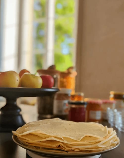 Pile de crêpes dans une assiette à la table du petit-déjeuner de La Maison D'olivier, avec des fruits frais et des confitures à proximité