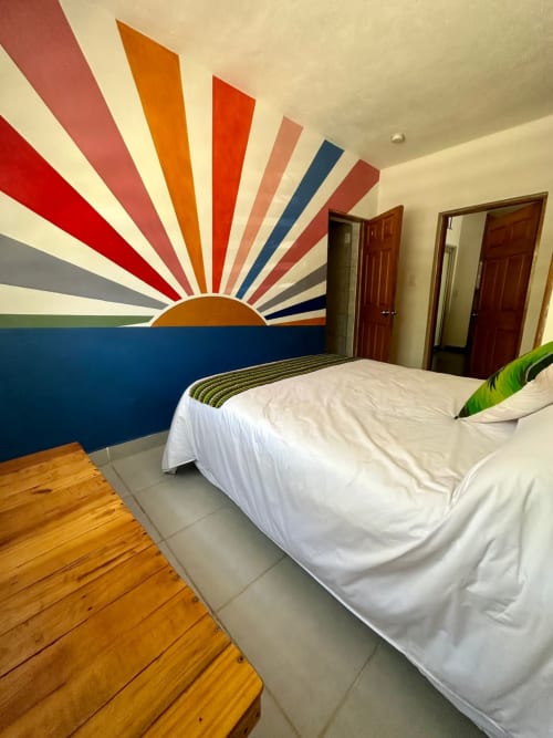 Mural colorido de amanecer en dormitorio moderno del Hotel Boutique BajaReal, La Paz, con cama blanca y detalles de madera