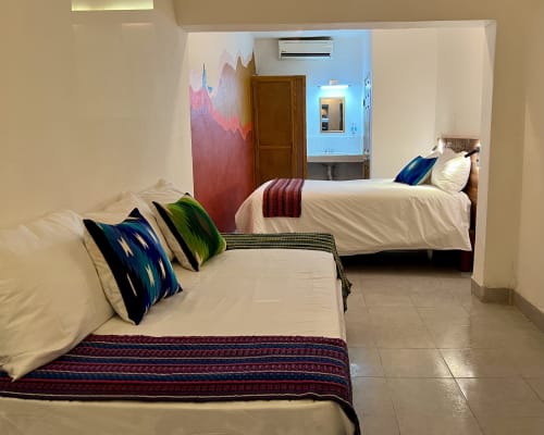 Dos camas con almohadas coloridas en BajaReal Hotel Boutique de La Paz, con obras de arte de montaña y comodidades modernas