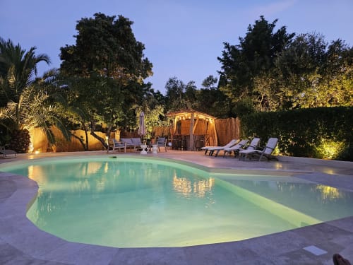 Illuminated infinity pool at Villa Sigahi in La Croix Valmer with lounge chairs and tropical garden at dusk