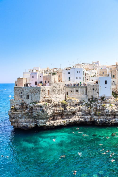 Villaggio mediterraneo in cima a una scogliera con edifici pastello colorati, acqua turchese cristallina e bagnanti a CorteLirice Paradiso
