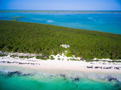 Vista aérea de la villa Hacienda Chekul en Tulum con aguas turquesas del Caribe, playa de arena blanca y exuberante vegetación selvática.