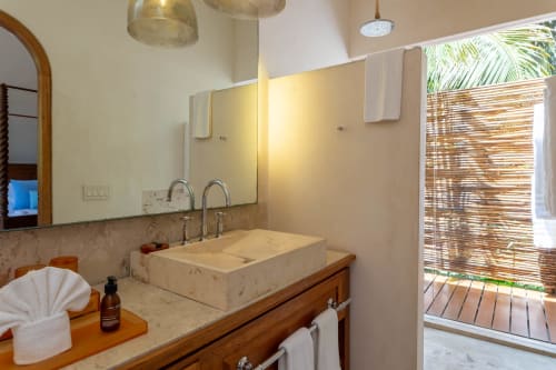 Lujoso baño de villa en Tulum con lavabo de mármol, grifería dual, espejo y acceso a ducha tropical al aire libre