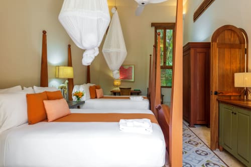 Habitación con dos camas individuales en villa de Hacienda Chekul, Tulum, con acentos naranjas, muebles de madera y mosquitero