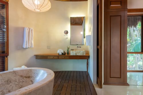 Baño lujoso en villa Hacienda Chekul del resort Tulum con bañera de piedra, tocador de madera, espejo y puertas con vista al océano