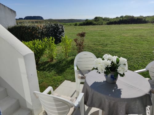 Chaises blanches et table avec fleurs donnant sur les champs verts de l'appartement Loc'Maria Belle Île en Mer