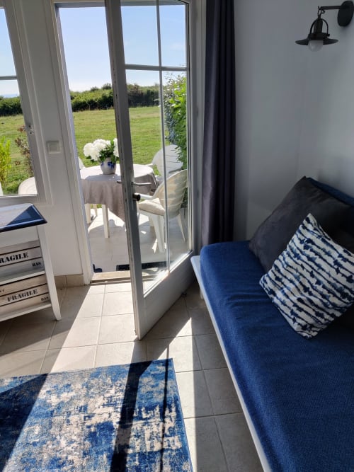 Chambre lumineuse avec canapé bleu et portes vitrées donnant sur les champs verts à Locmaria, Belle Île en Mer