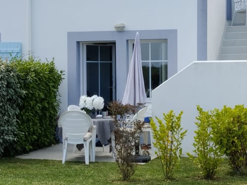 Terrasse ensoleillée de l'appartement Loc'Maria Belle Île-en-Mer avec chaises blanches, table, parasol et jardin aménagé