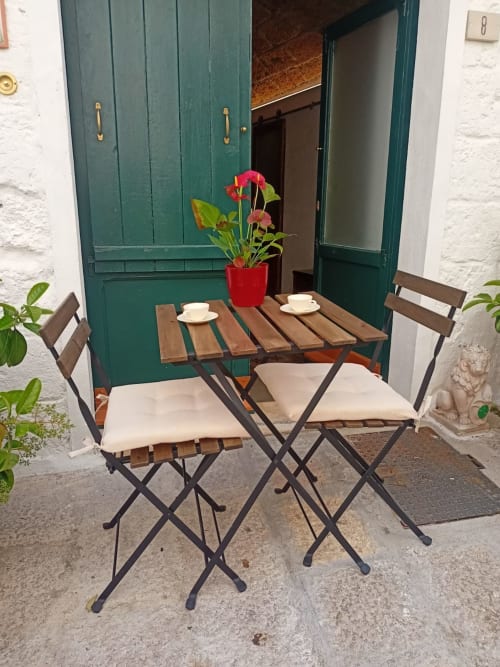 Outdoor seating area at CorteLirice Paradiso with wooden table, two chairs with cushions, coffee cups, and red flowers by