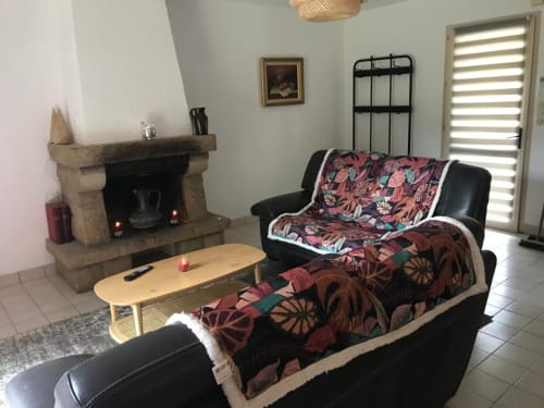 Salon cosy au Village Du Moulin avec cheminée, canapés en cuir noir, plaids à motifs et table basse en bois
